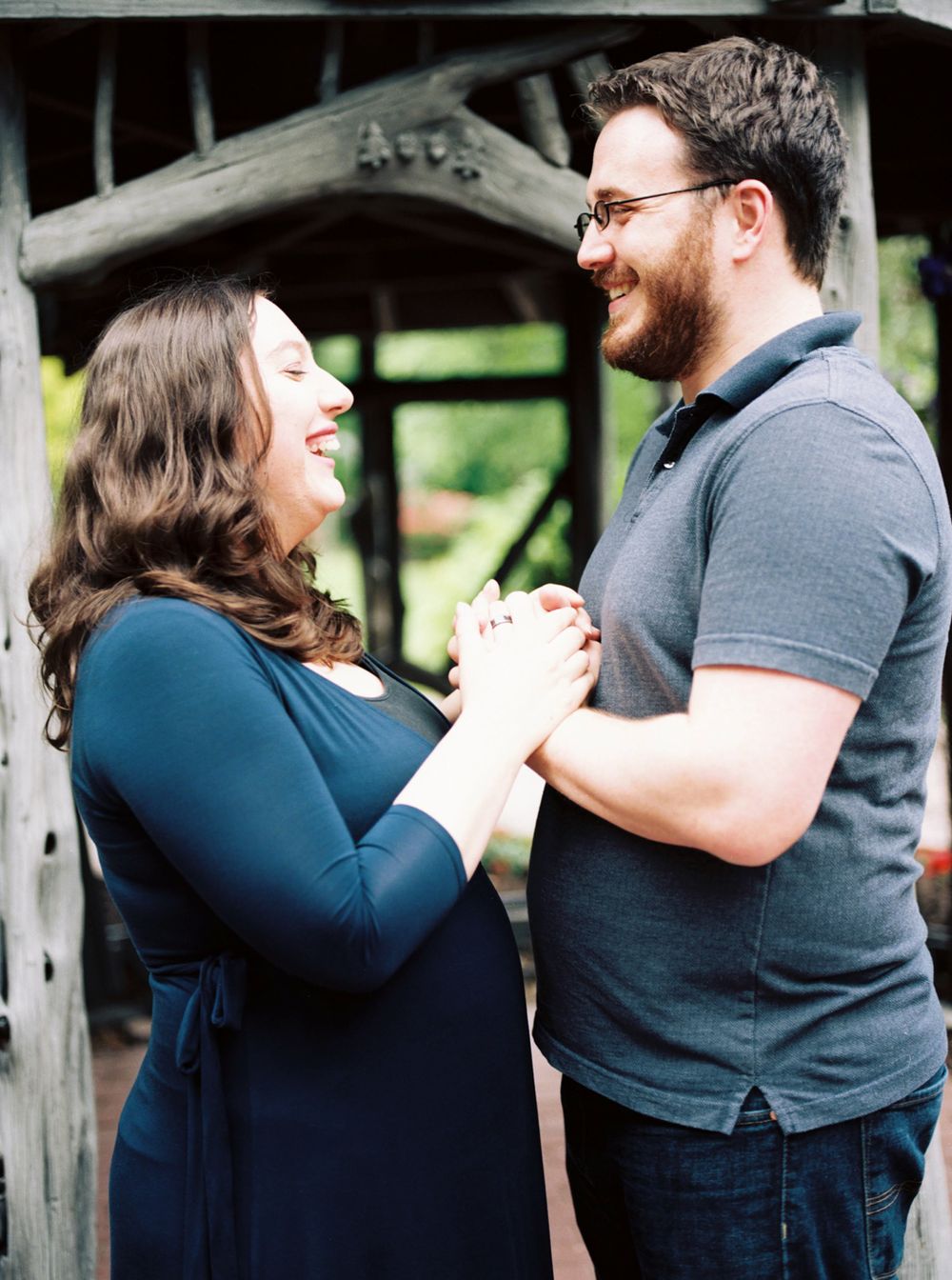 Joyful couple laughing and holding hands under wooden archway.