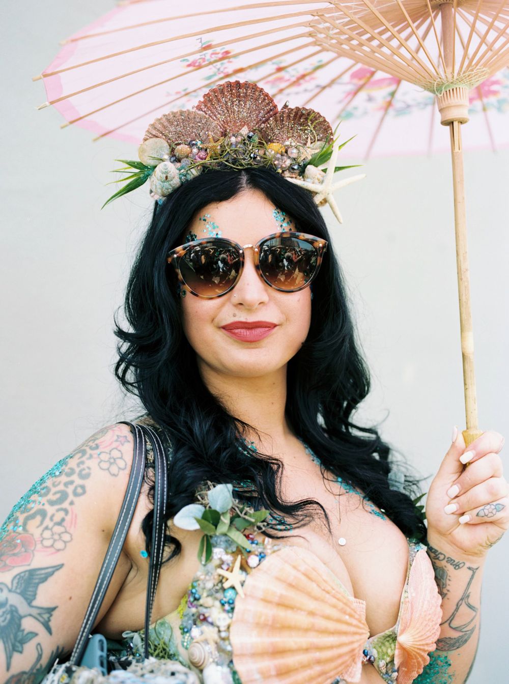 Stylish festival-goer with parasol wearing ornate headpiece and sunglasses.