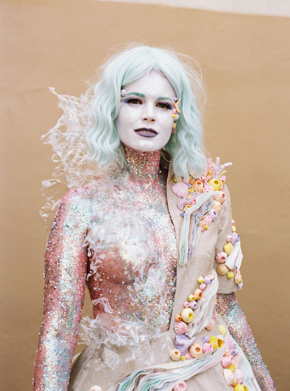 Ethereal fantasy portrait with glitter makeup and mint hair against beige background.