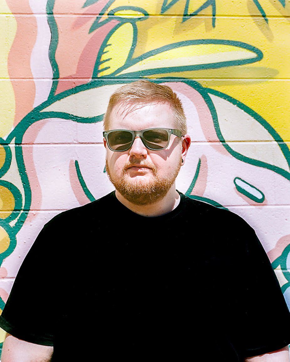 A person in sunglasses poses against a colorful graffiti wall with cartoon characters.
