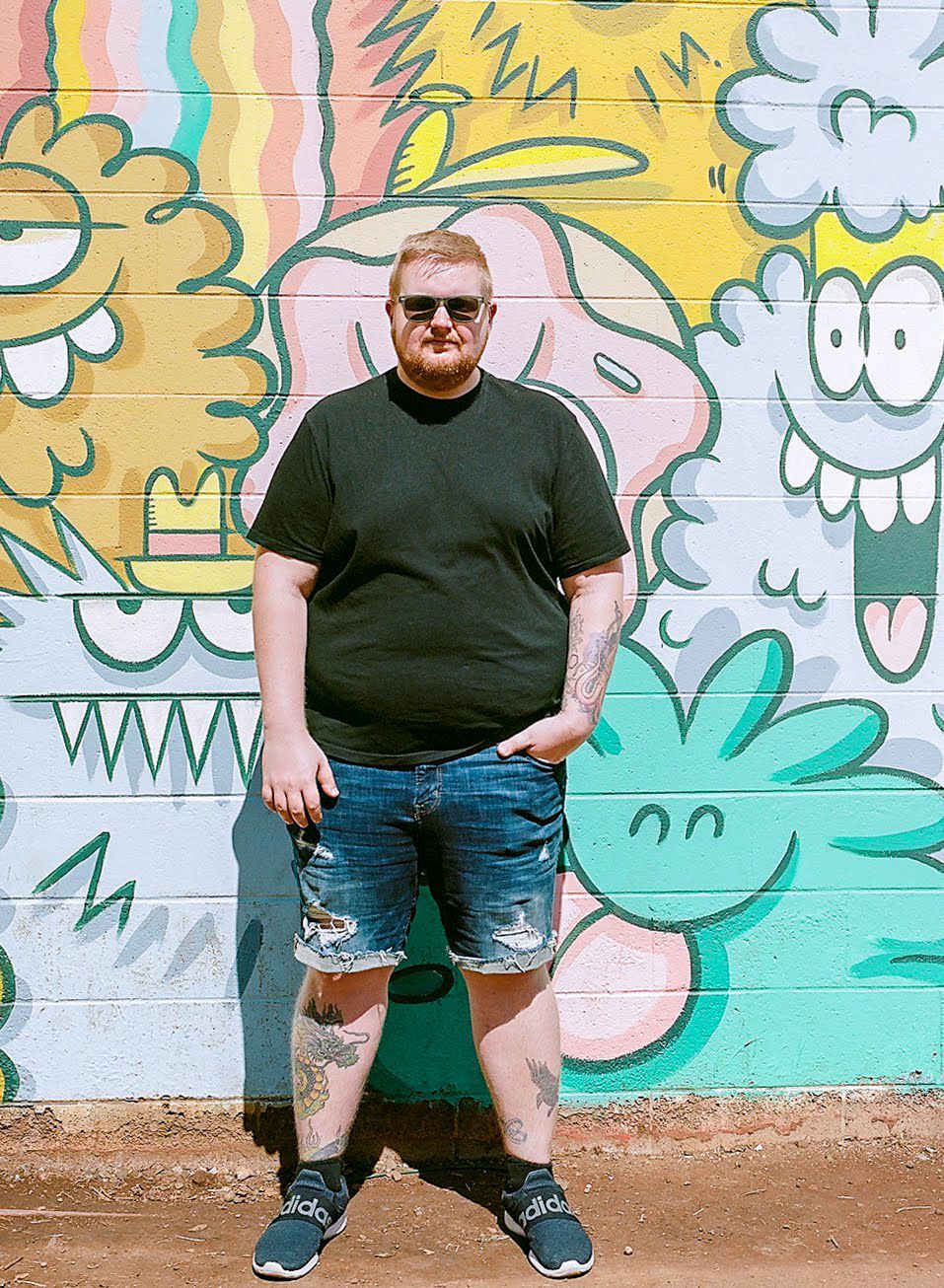 A person in casual wear stands against a wall decorated with playful cartoon graffiti art.