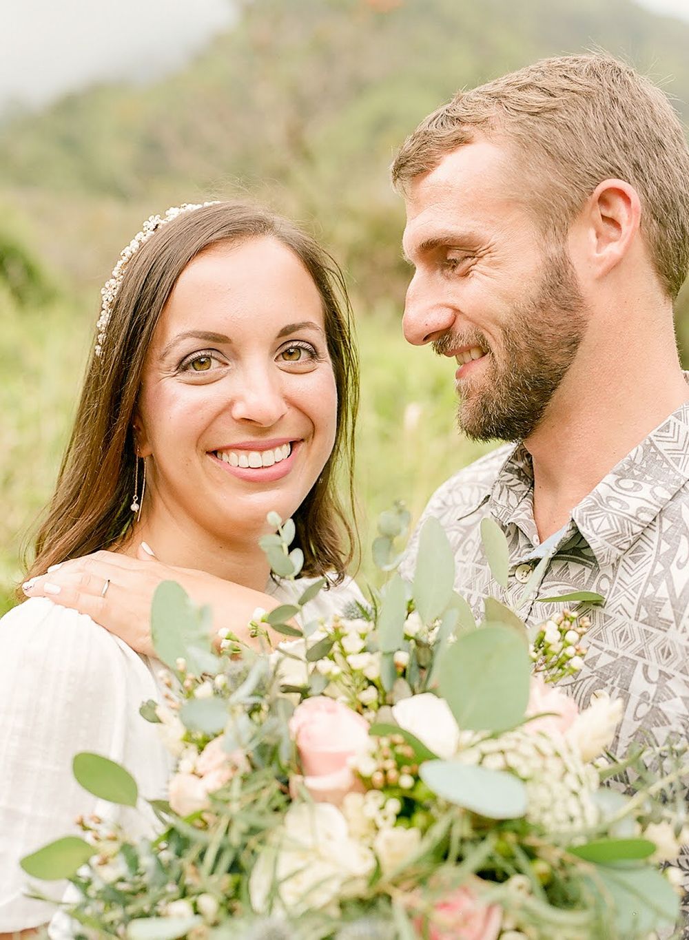 An intimate portrait of a couple with a floral bouquet in a natural outdoor setting.
