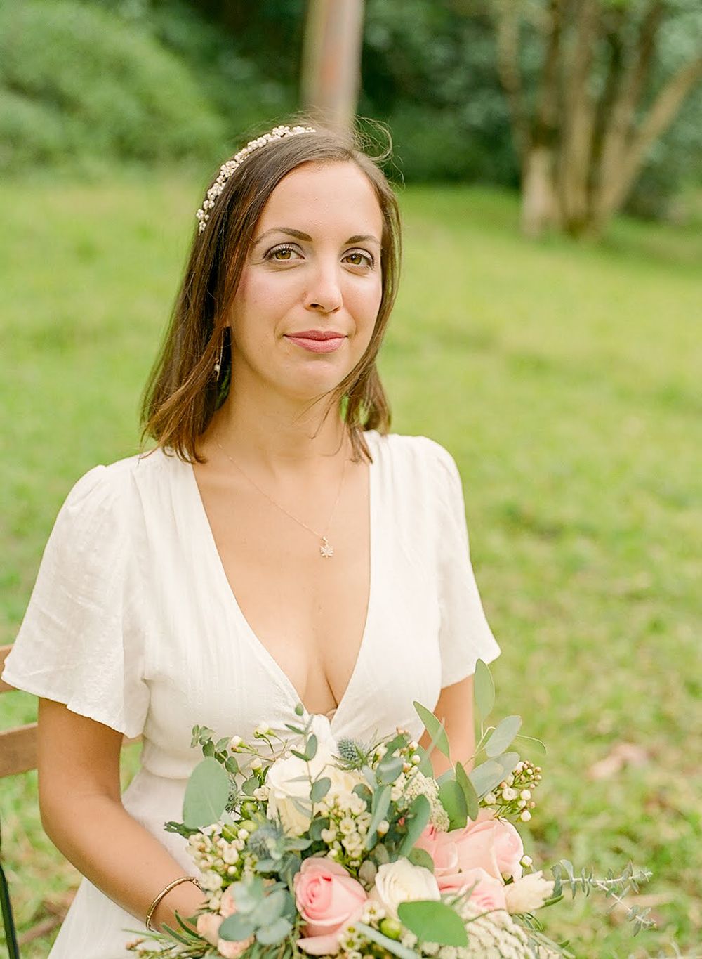 A bride holds a beautiful bouquet of roses and greenery in an outdoor garden setting.