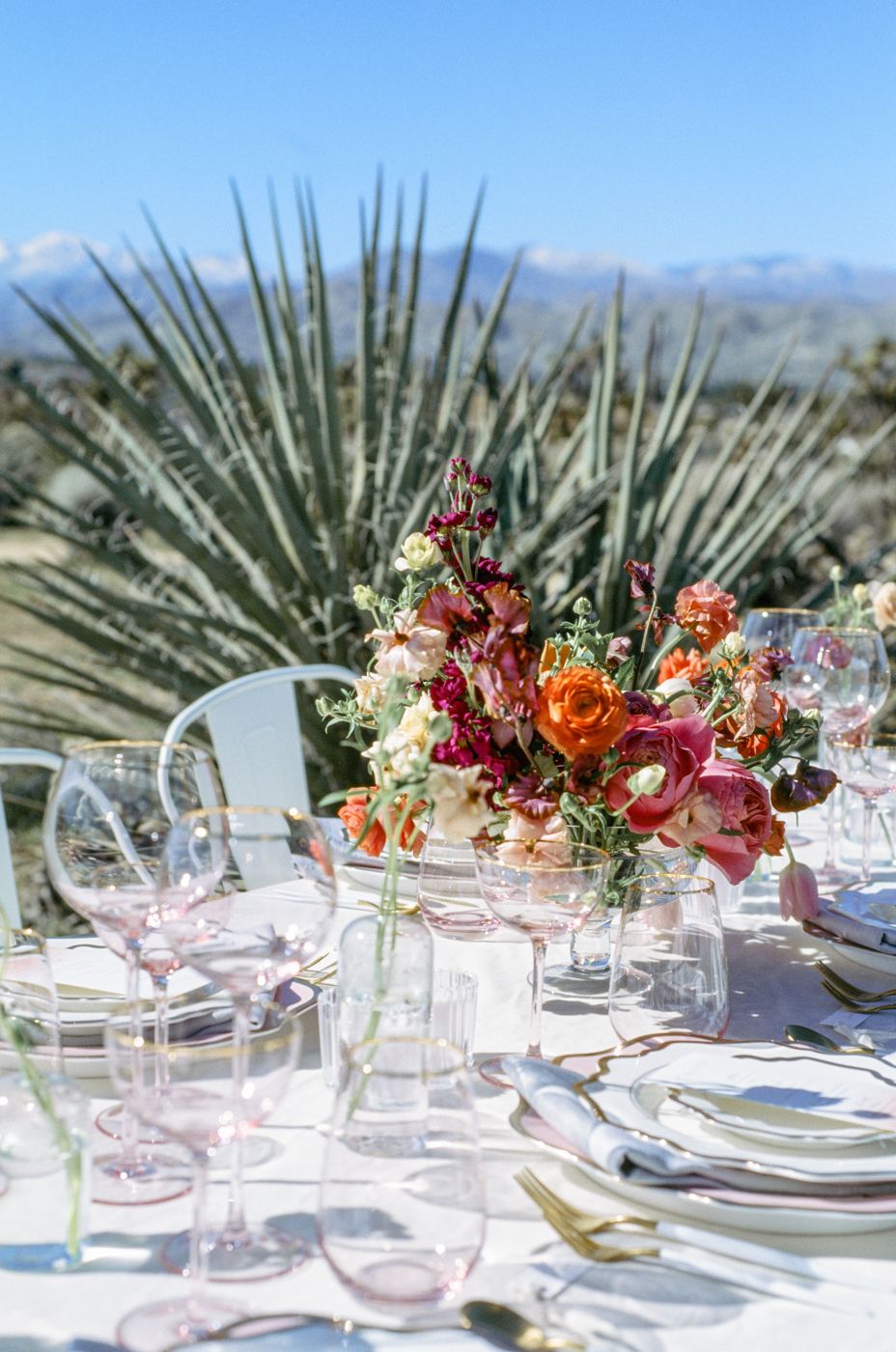 An elegant table setting with colorful floral centerpiece and pink glassware against desert landscape.