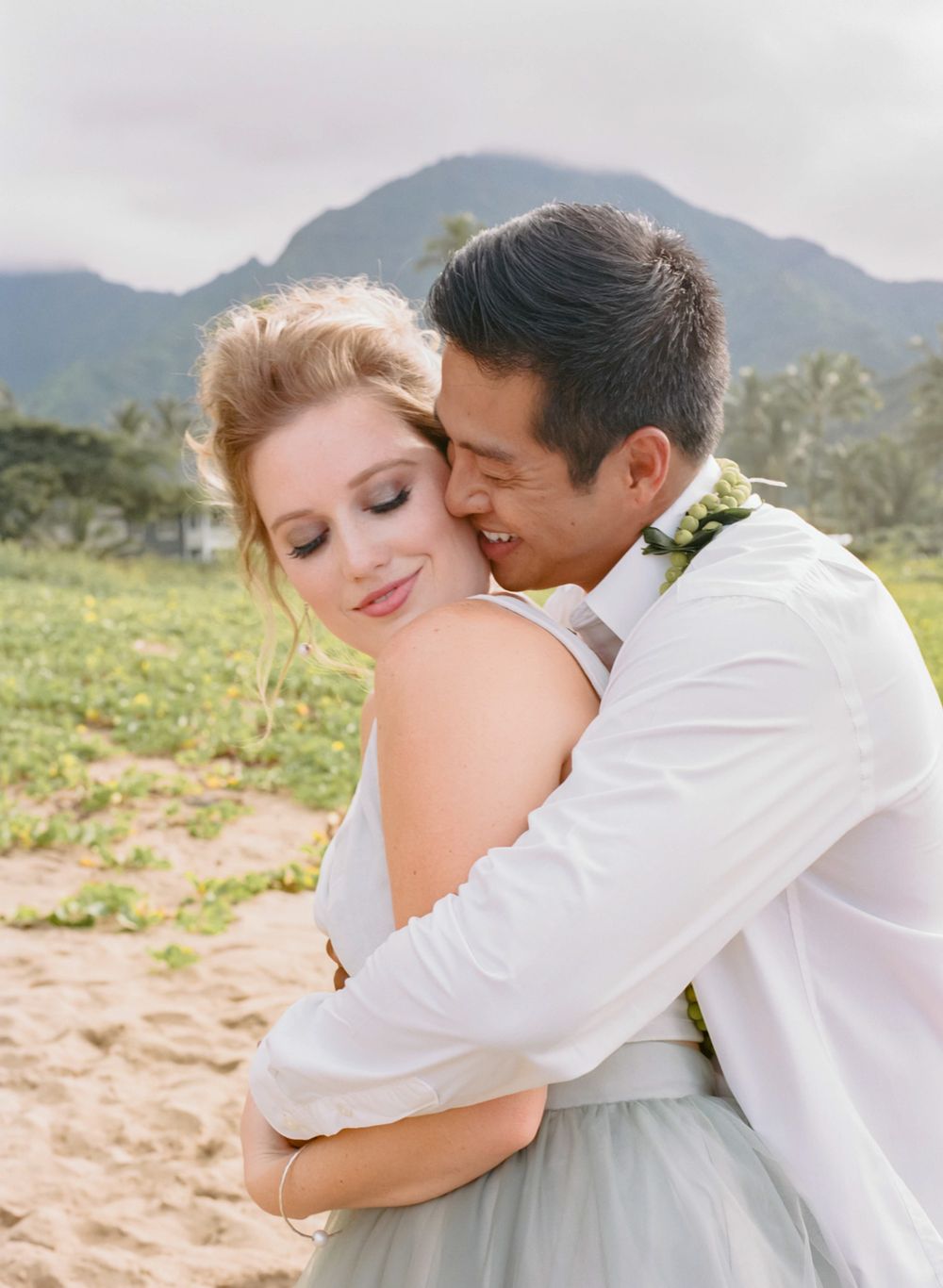 Intimate wedding couple embrace against mountain backdrop during golden hour photography session.