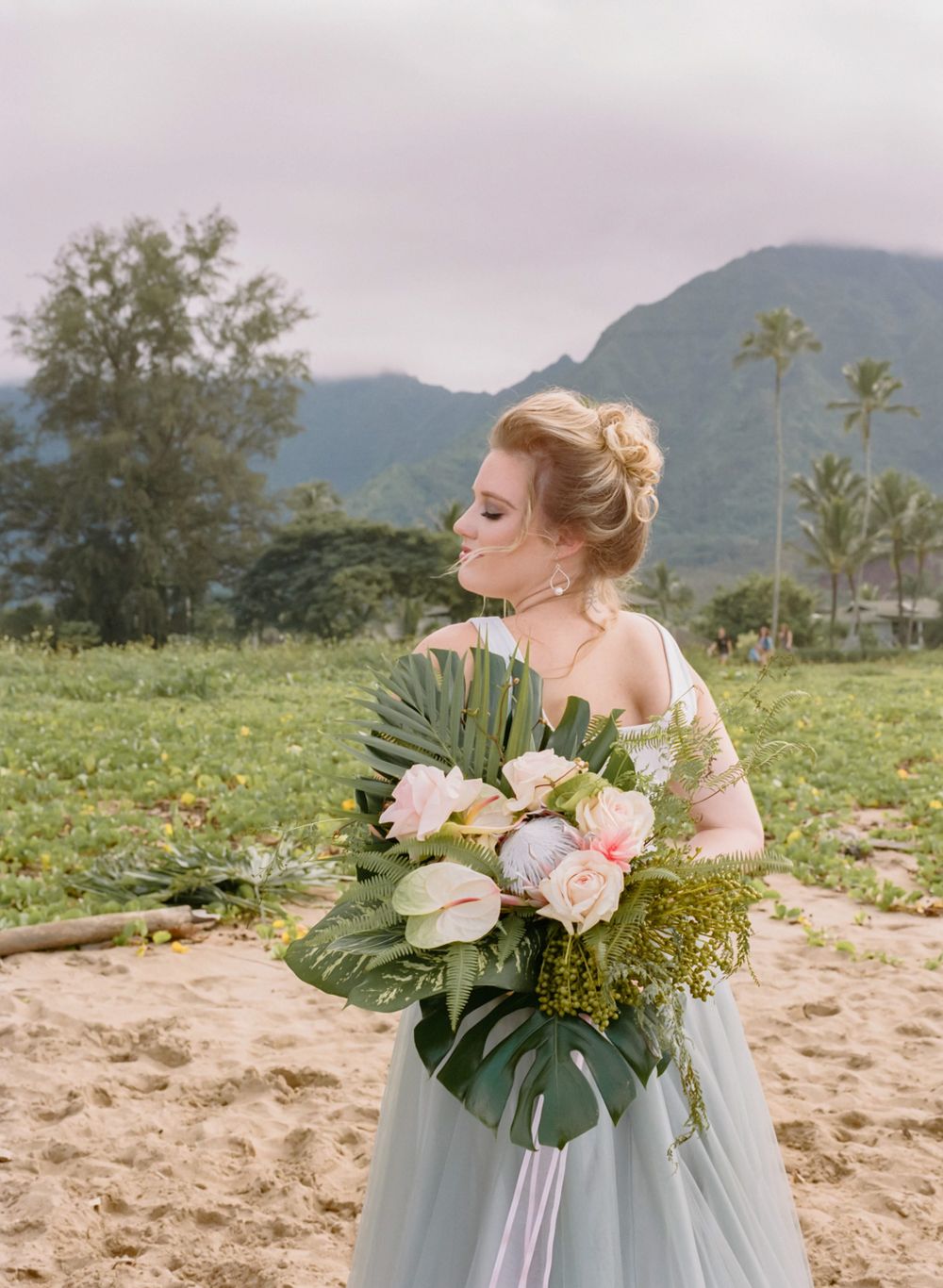 Bride in tulle gown holds tropical bouquet featuring anthuriums and roses.