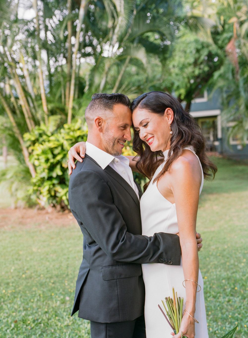 Elegant couple shares tender moment in lush tropical garden during wedding portraits.