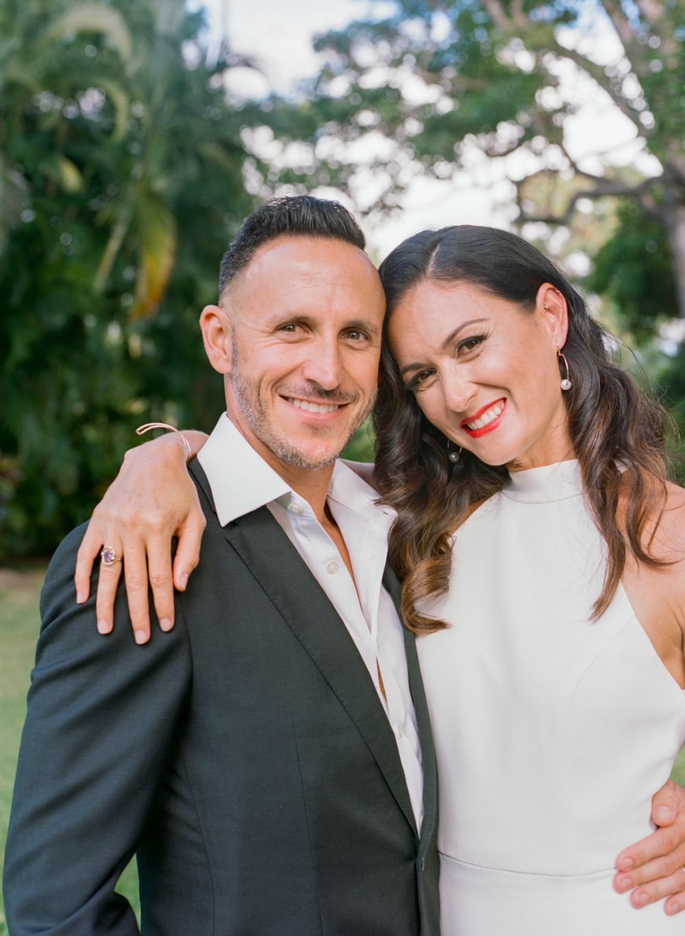 Happy couple poses for portrait in tropical garden setting wearing formal attire.
