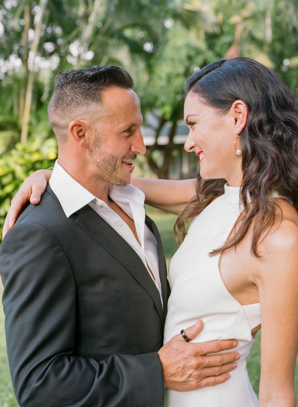 Wedding couple shares intimate laugh during outdoor garden photoshoot.