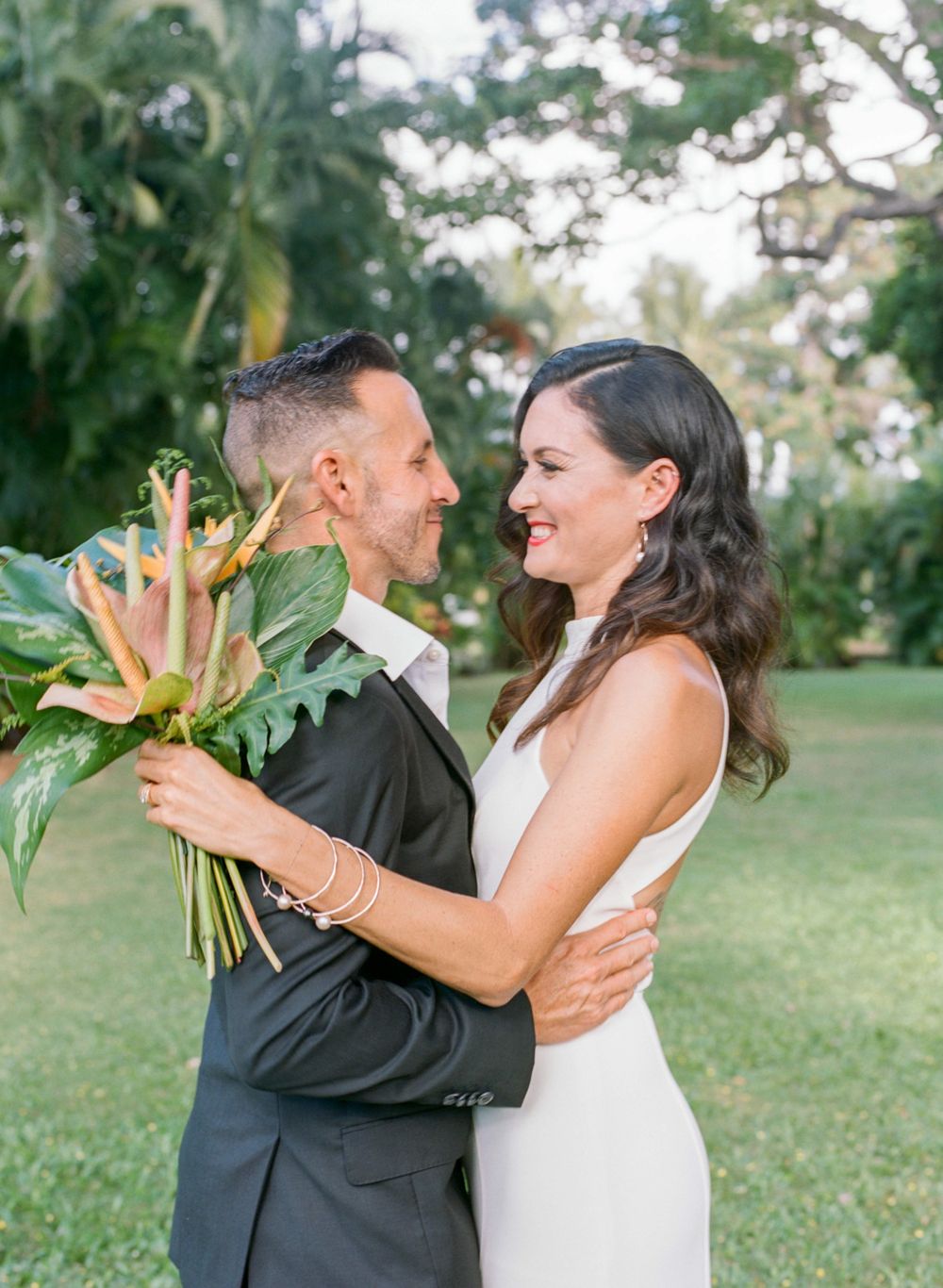 Couple shares romantic moment with tropical bouquet in garden setting.