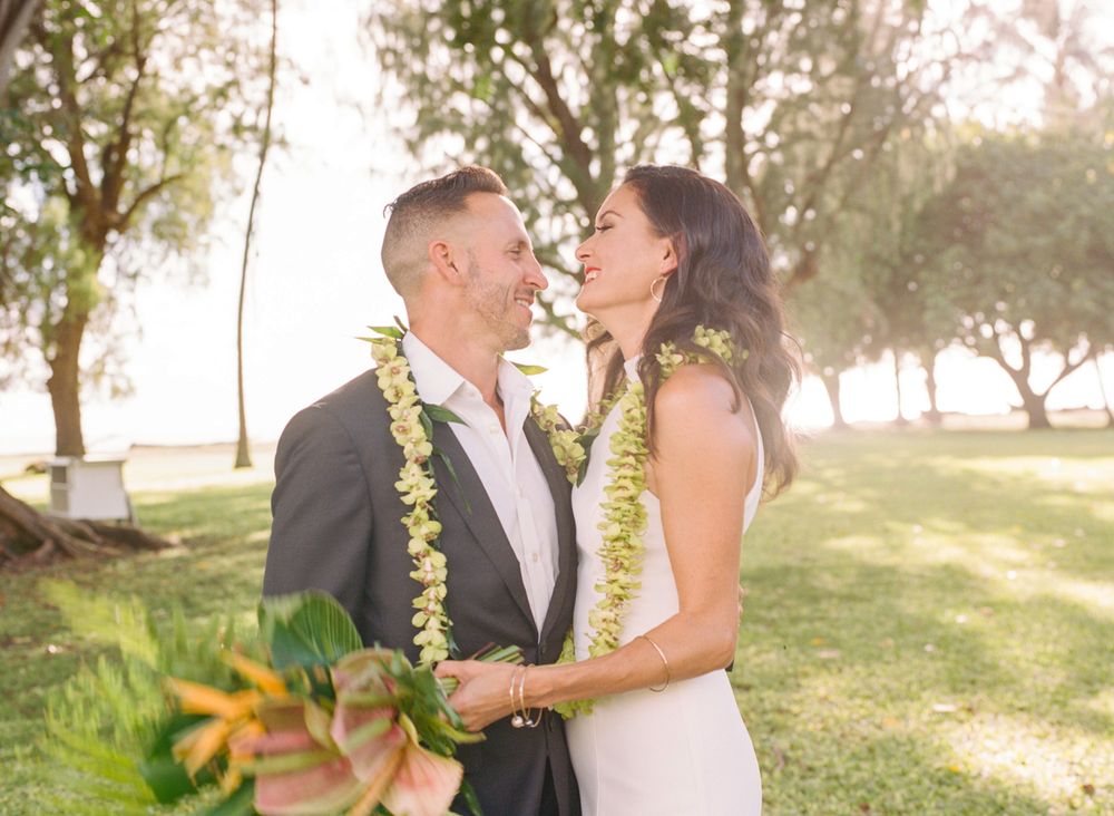 Couple shares joyful moment wearing leis during outdoor wedding ceremony.