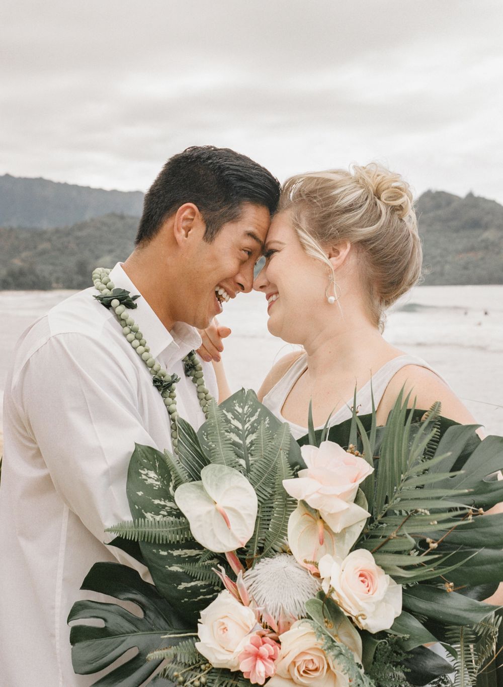 Intimate wedding moment captured with tropical bouquet and ocean view.