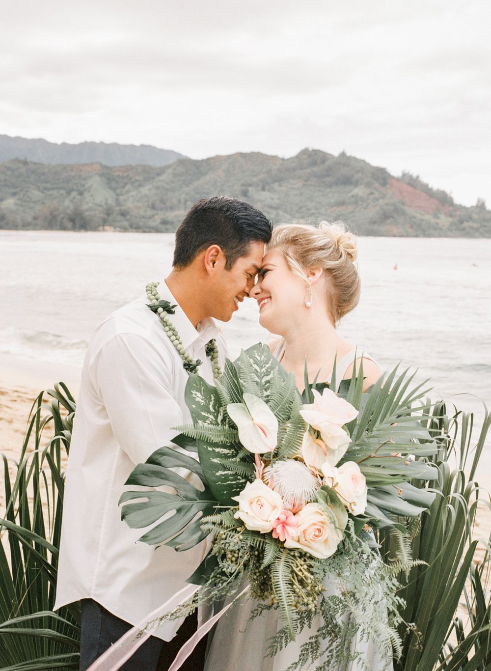 Romantic coastal wedding portrait featuring tropical florals and mountain backdrop.