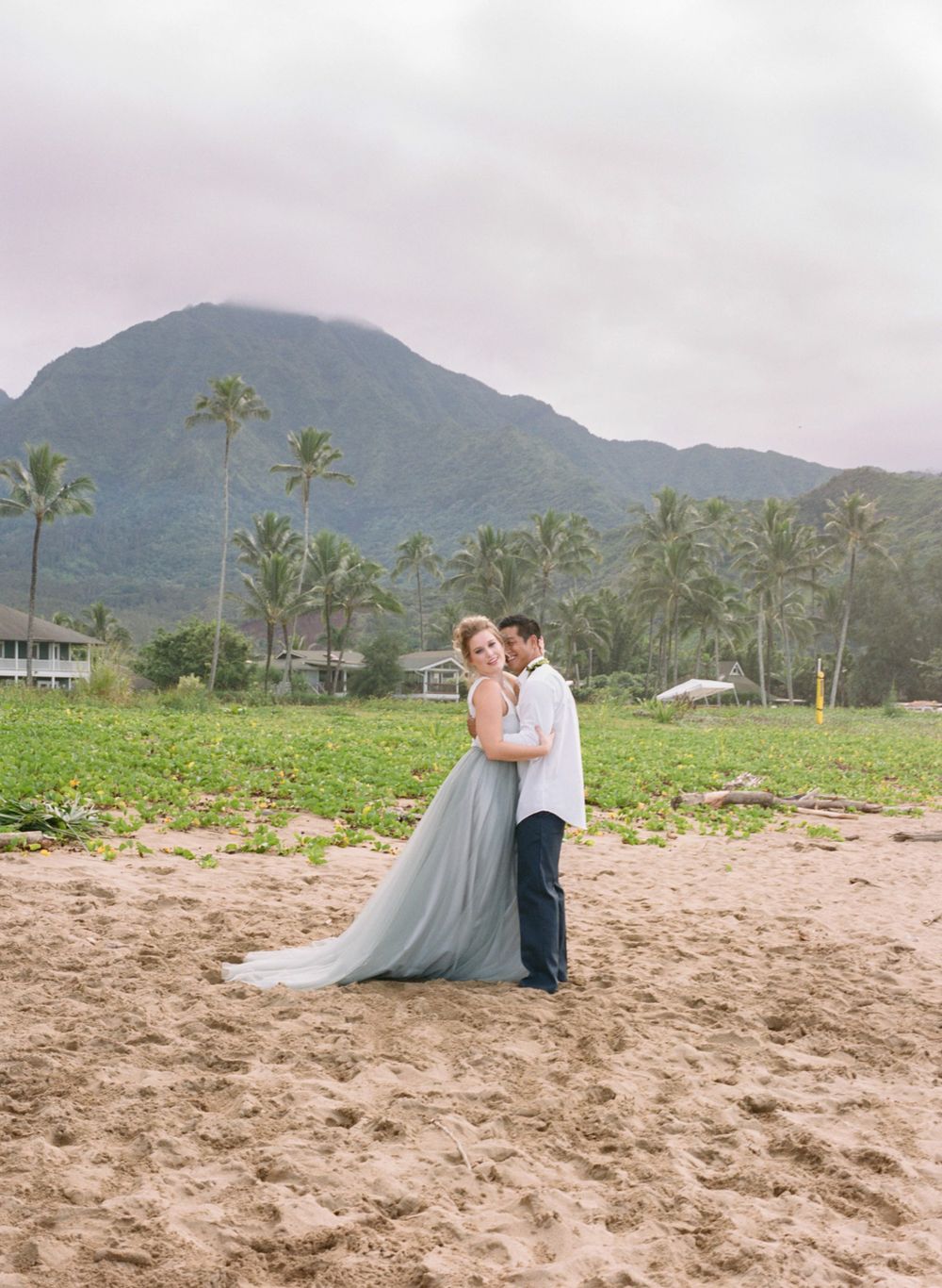 Beach wedding portrait with majestic mountain backdrop and palm trees.