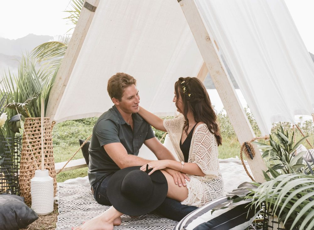 Intimate glamping scene with couple sitting inside decorated A-frame tent.