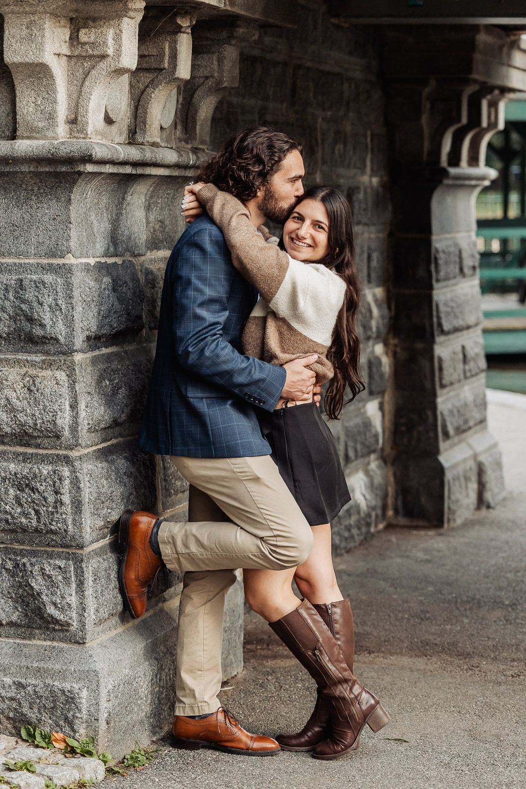 A couple sharing an intimate moment against a stone column wearing complementary fall outfits.