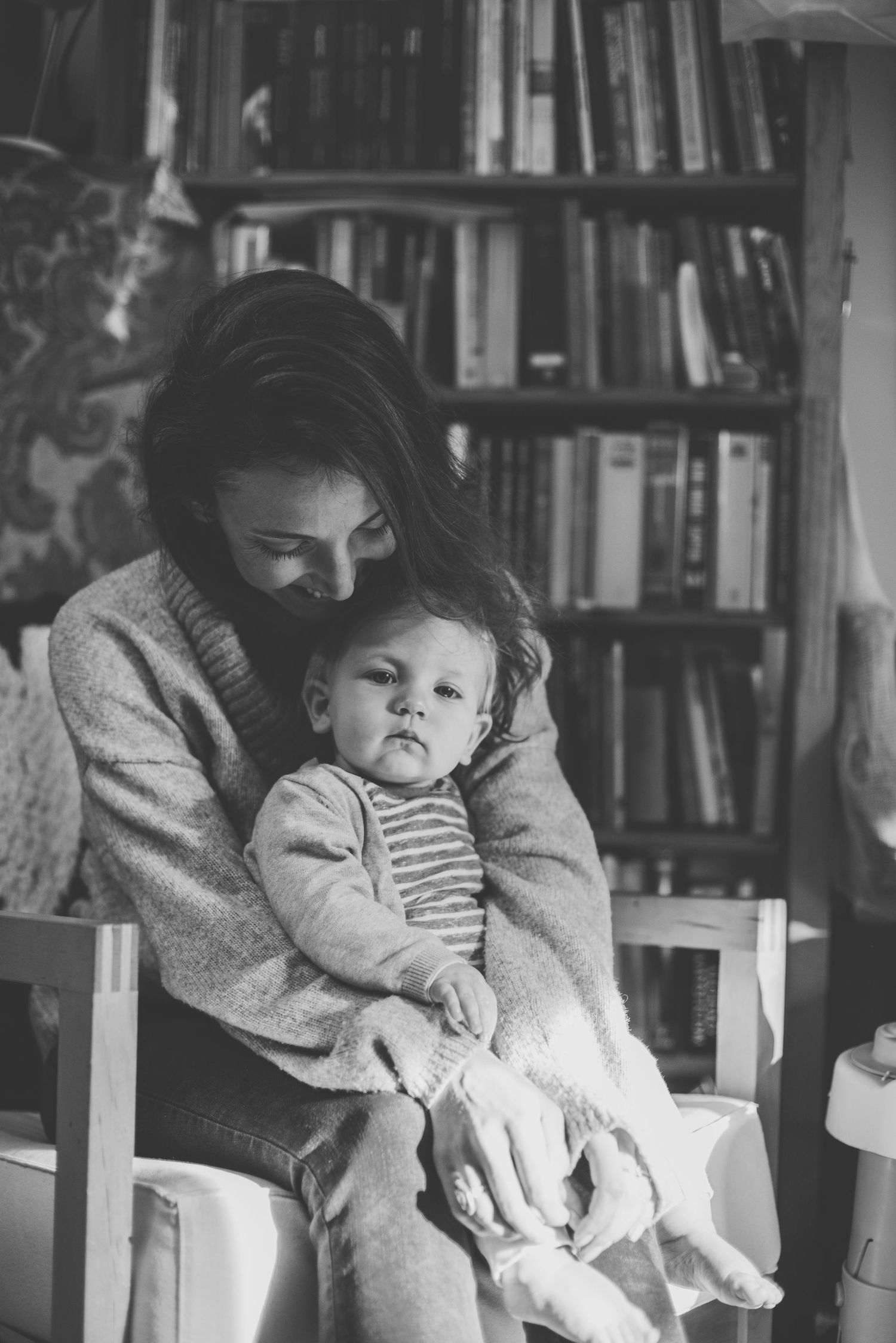 A tender black and white moment between mother and baby son in a cozy home library setting with bookshelves in the background.
