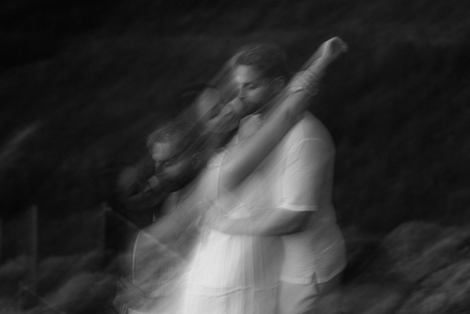 Artistic blurred black and white portrait capturing ethereal movement in white dress against dark background. Tenerife Wedding Photographer