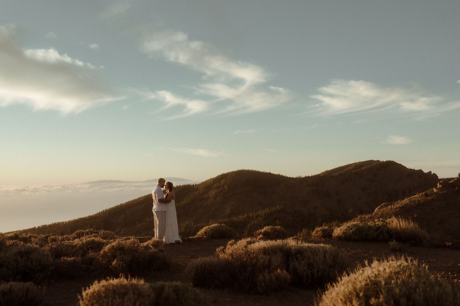 Couple in wedding attire stands silhouetted against mountain landscape at golden hour. Tenerife Wedding Photographer at Teide.