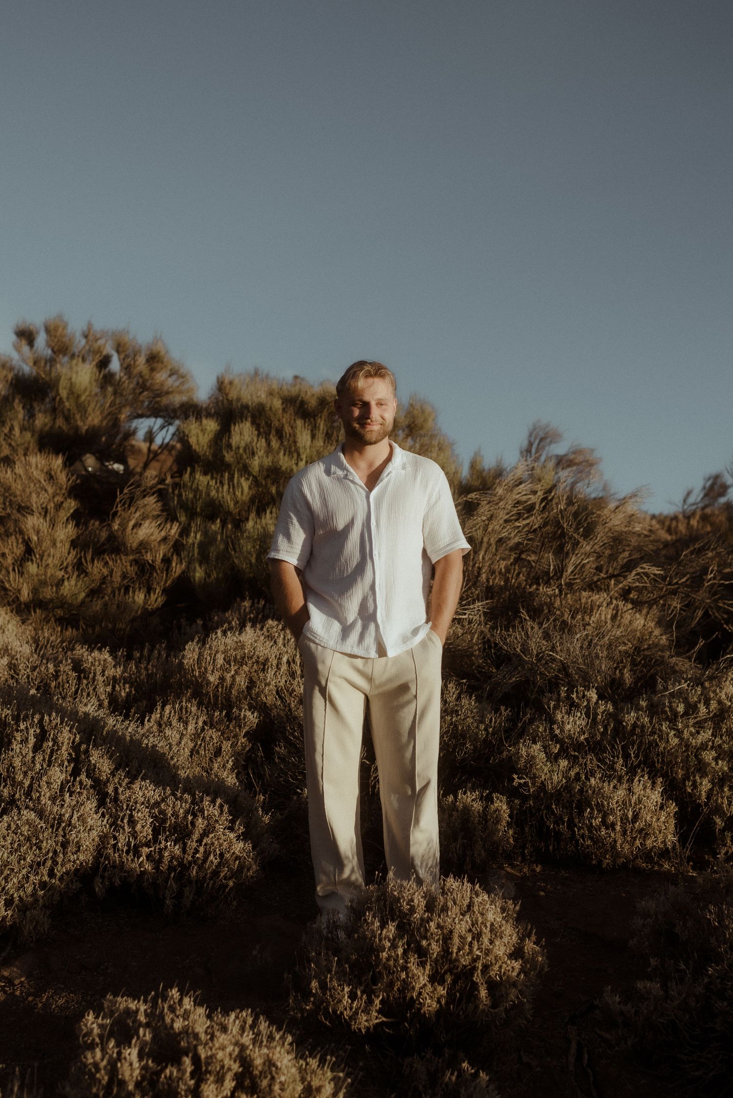 Person in all white clothing stands among desert brush during golden hour. Tenerife Wedding Photographer at Teide.
