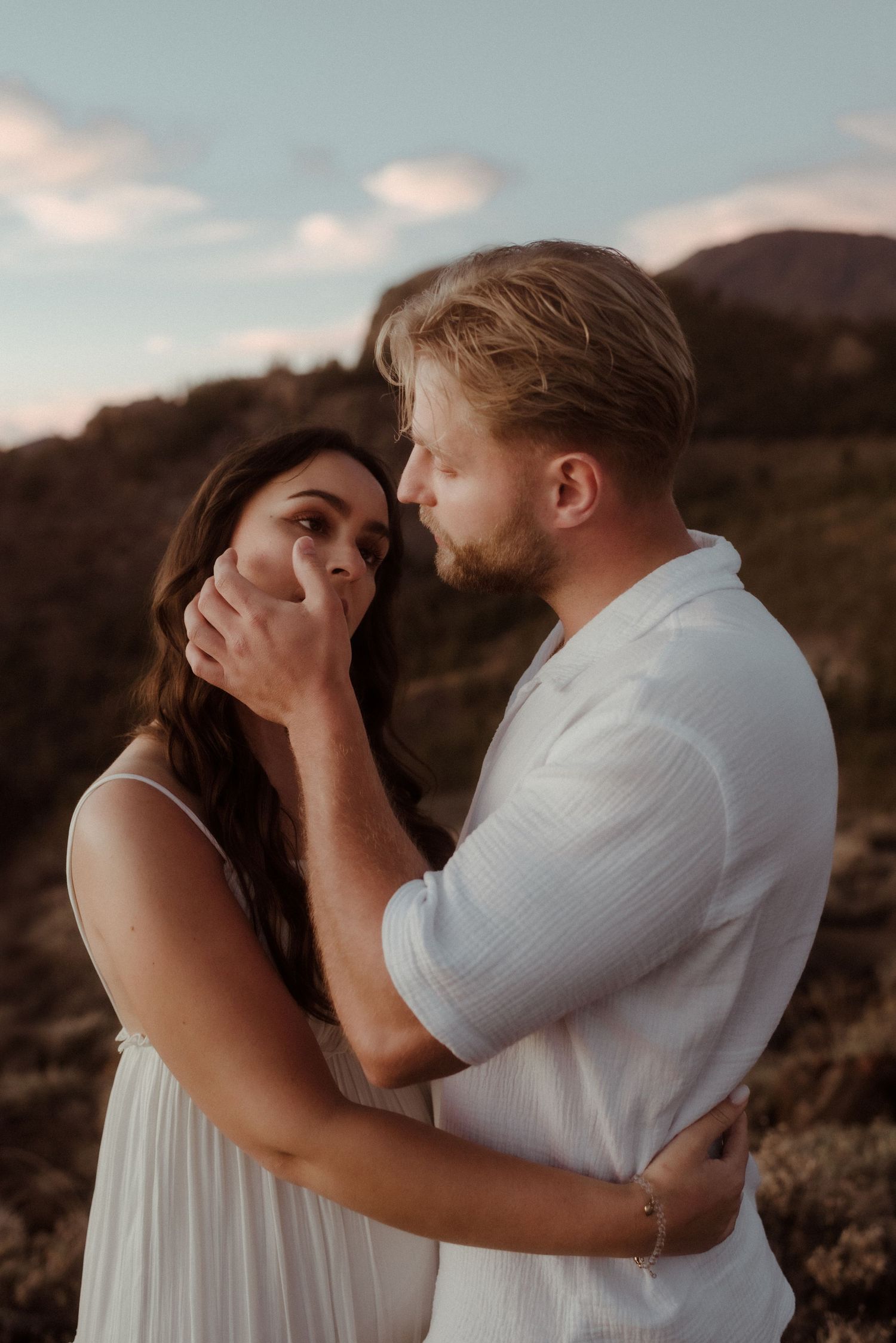 Couple in white embraces against dramatic mountain landscape during sunset photography session. Tenerife Wedding Photographer at Teide.