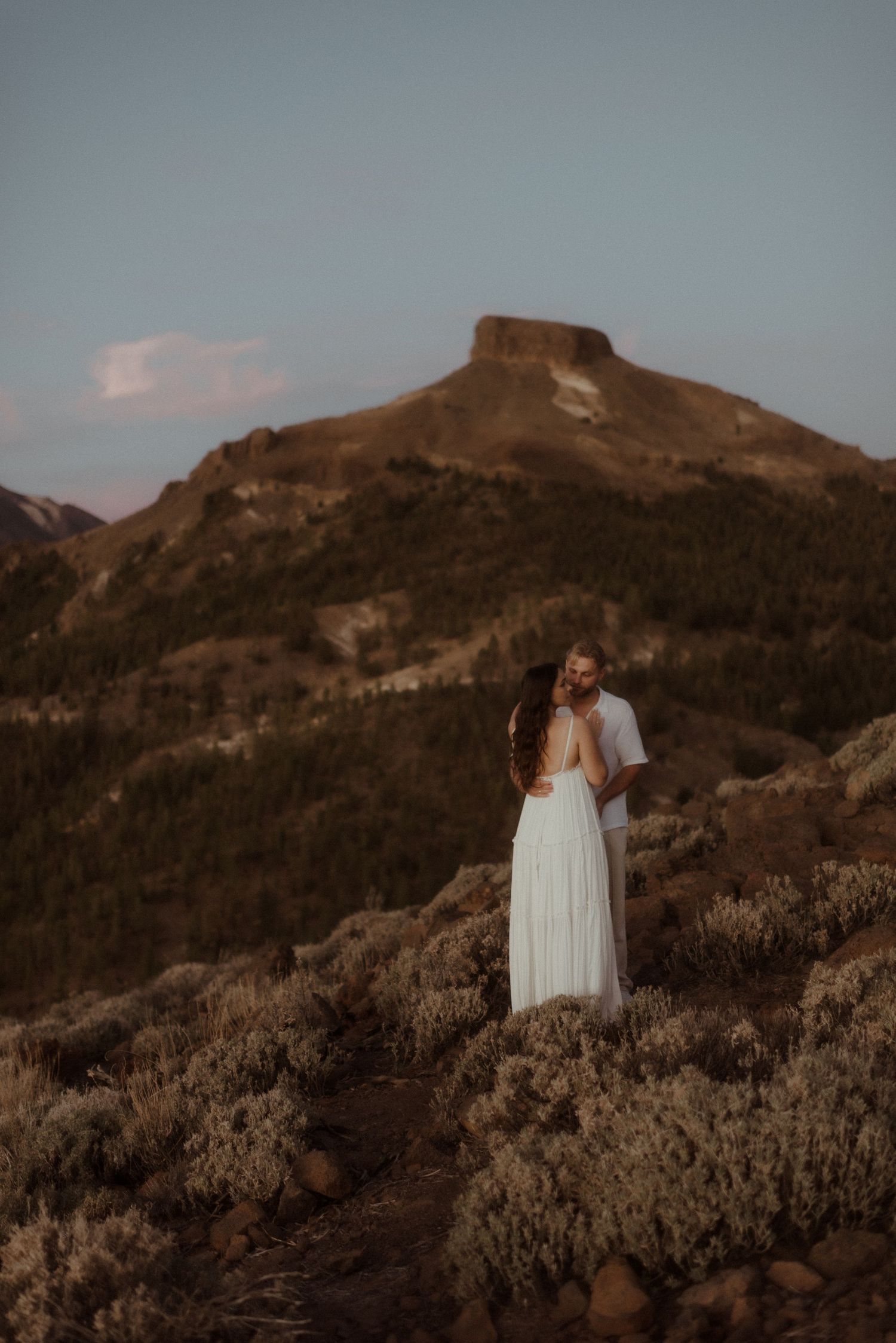 Couple in white stands together on mountain trail with dramatic peak in background. Tenerife Wedding Photographer at Teide.