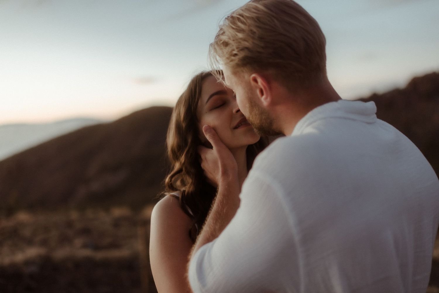 An intimate moment between a couple in white against a mountainous backdrop at dusk. Tenerife Wedding Photographer at Teide.