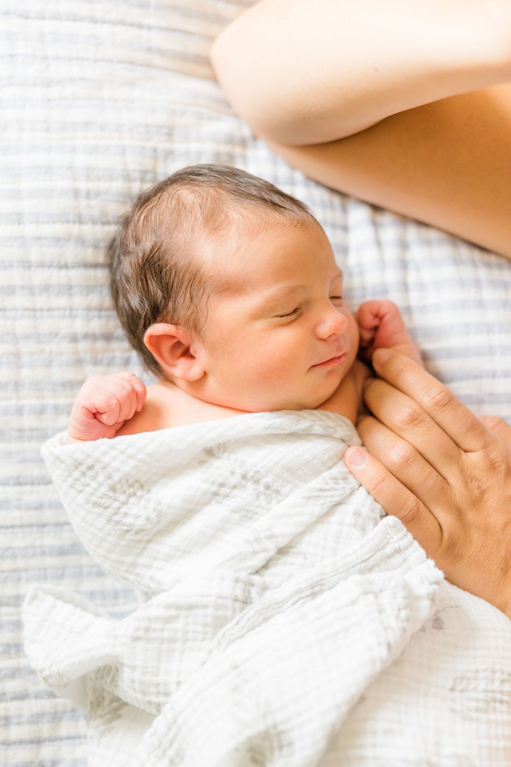 A sleeping newborn baby swaddled in white fabric rests peacefully on soft bedding.