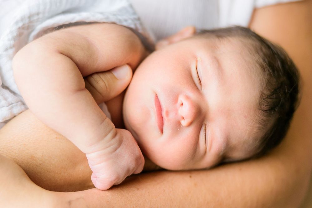 Peaceful sleeping infant with dark hair rests curled up against soft skin.