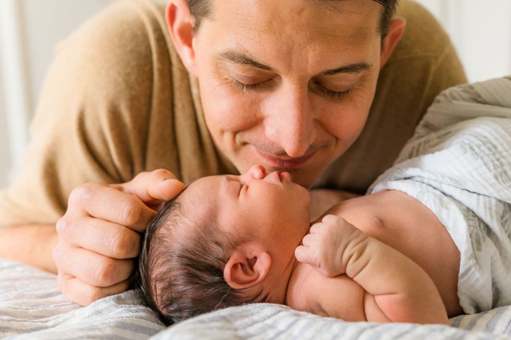 A tender moment between parent and newborn baby laying on white bedding.