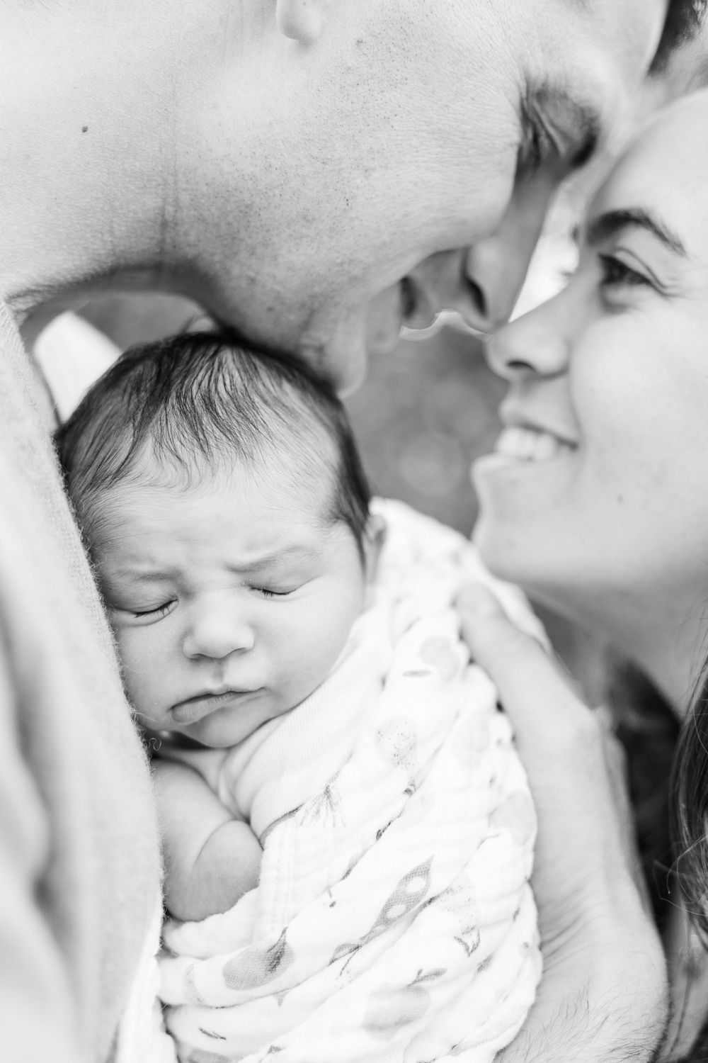 Black and white portrait of a peaceful sleeping newborn baby being lovingly held in a tender family moment.