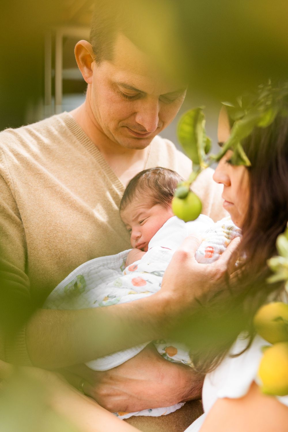 A tender family moment outdoors with a newborn baby nestled between two people in natural lighting.