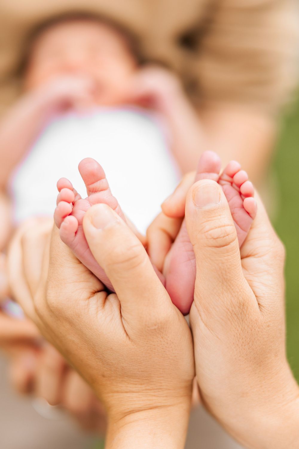 Gentle hands cradle tiny newborn baby feet against a soft blurred background.