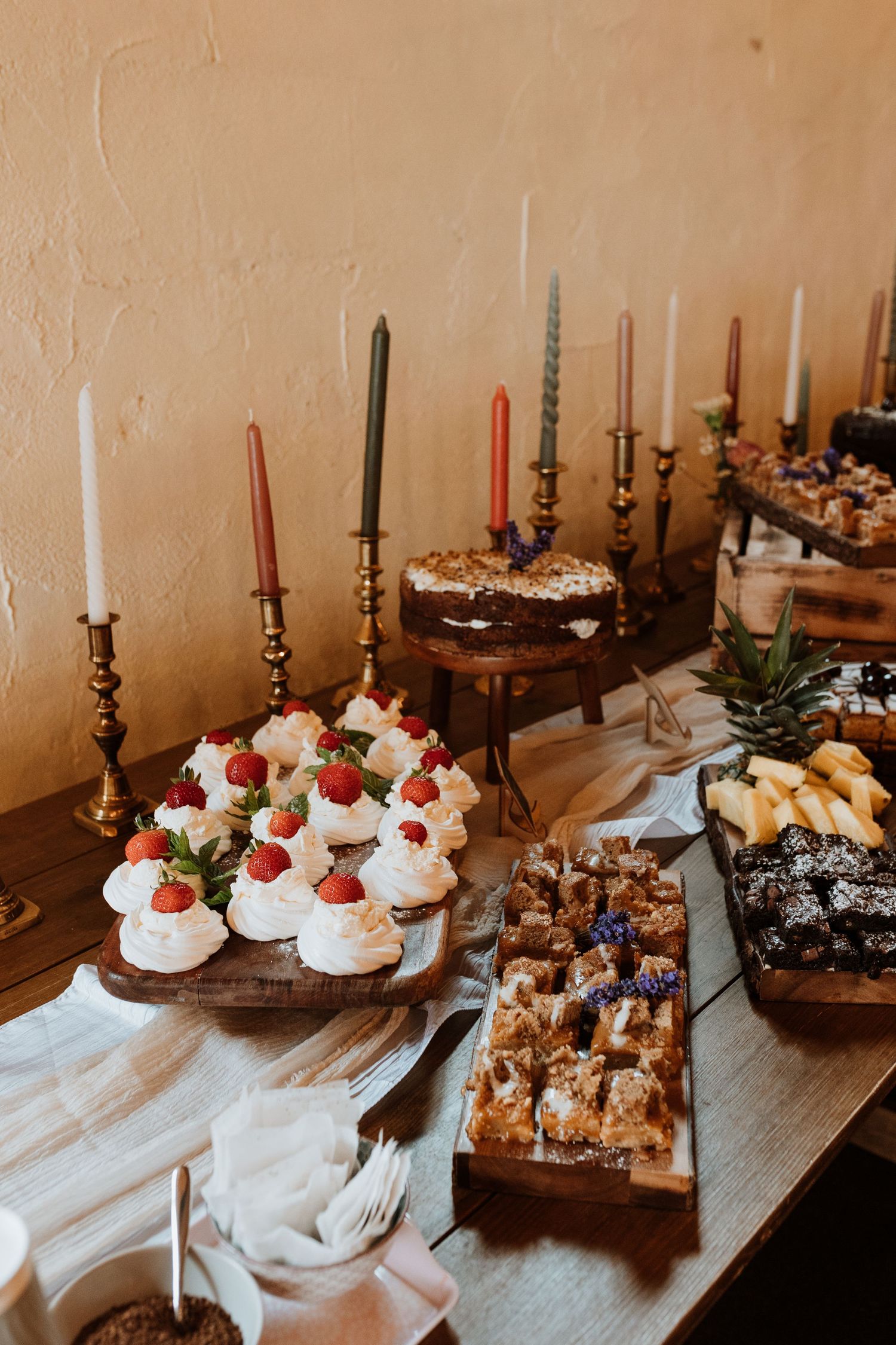 Elegant dessert table with meringues, strawberries, and pastries arranged on wooden boards with tall tapered candles.