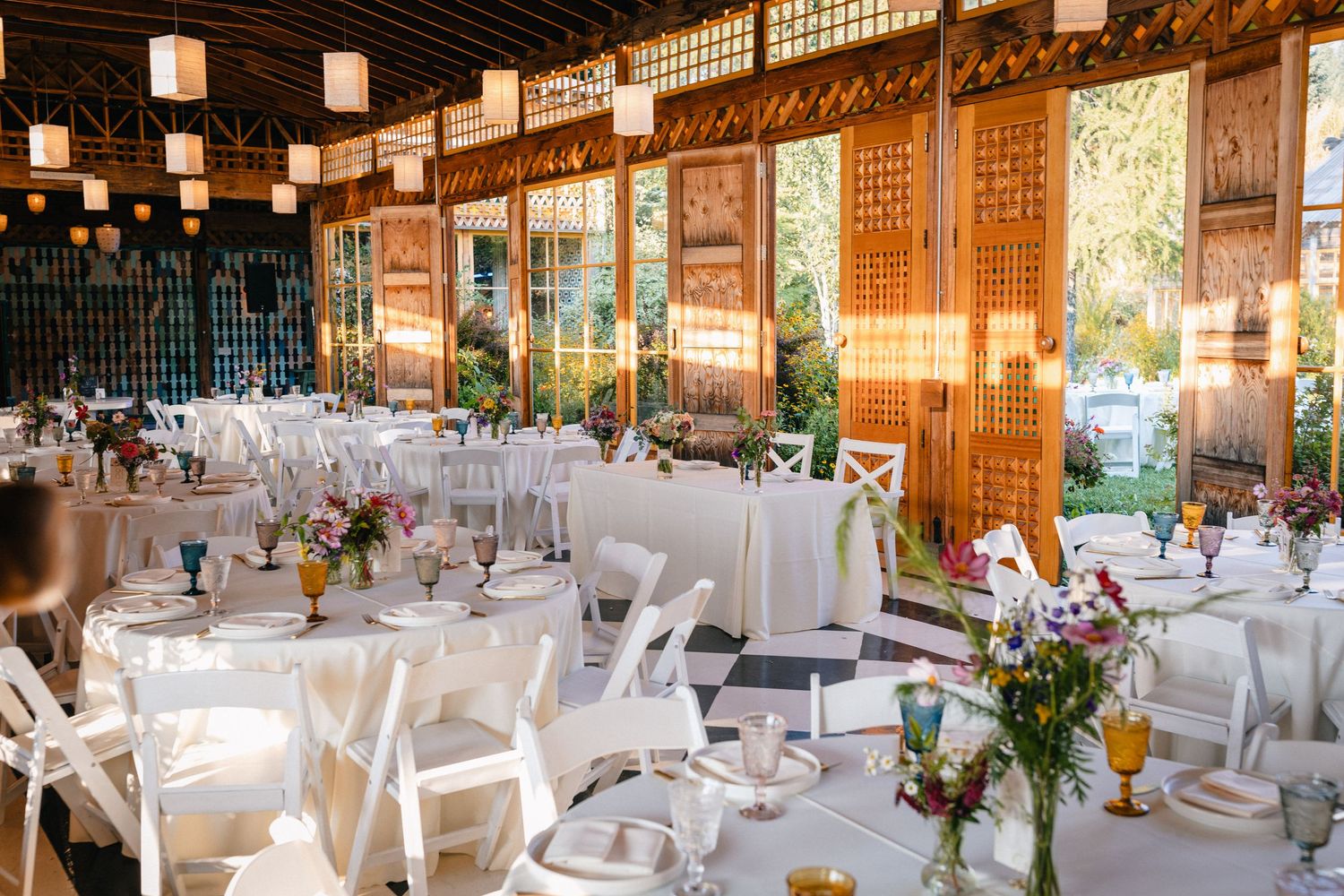 Wedding reception venue with elegant white tables, floral centerpieces and rustic wooden walls decorated with lanterns.
