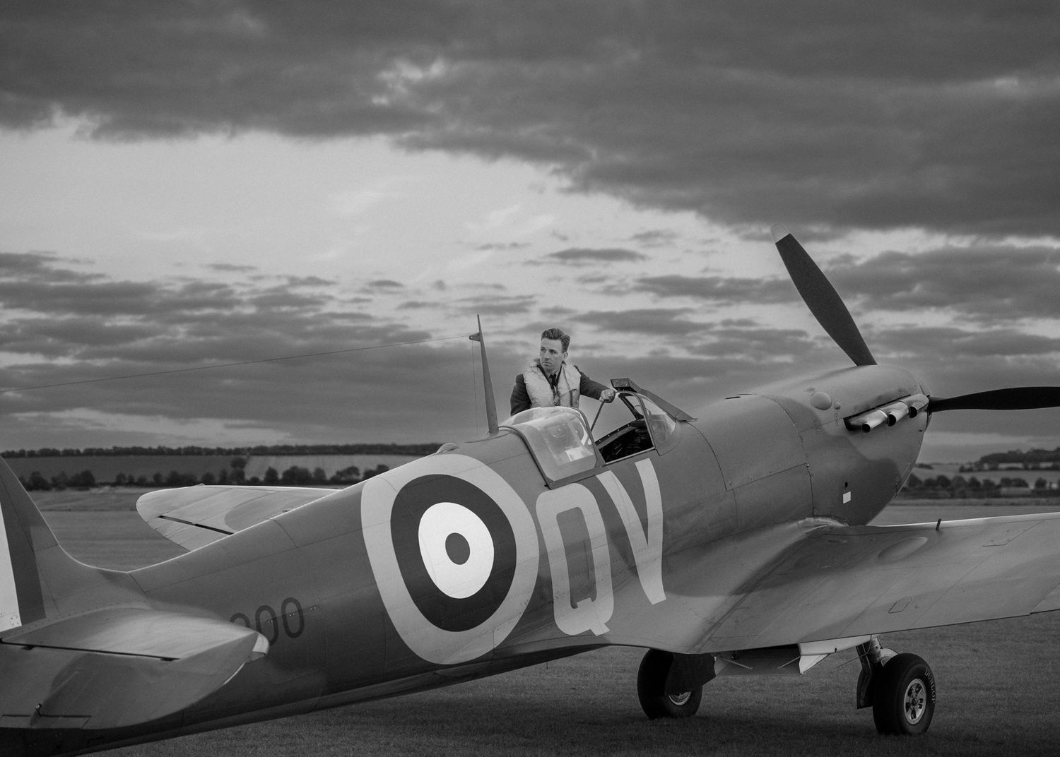A vintage RAF Spitfire aircraft with distinctive roundel markings parked on an airfield under dramatic clouds.