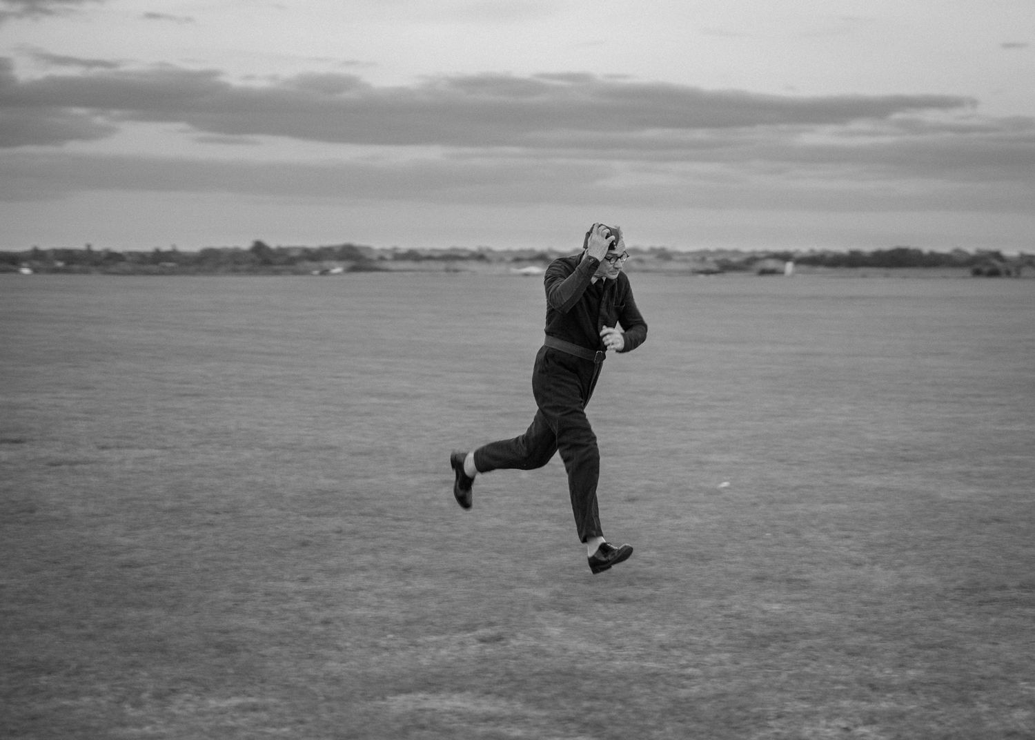 A figure runs across an empty airfield in black and white photography.