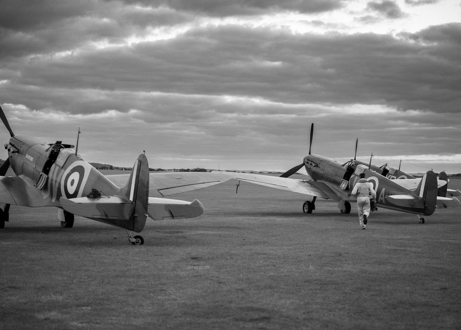 Multiple RAF Spitfire aircraft lined up on a wartime airfield under dramatic skies.