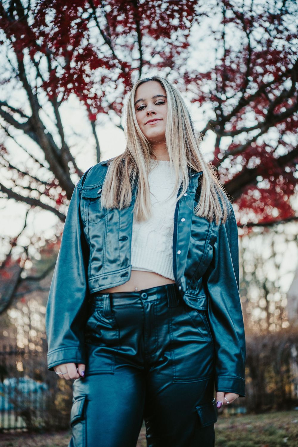 Someone wearing a blue denim jacket and pants poses outdoors against autumn foliage with red leaves in bokeh effect at Wall Park in MD.
