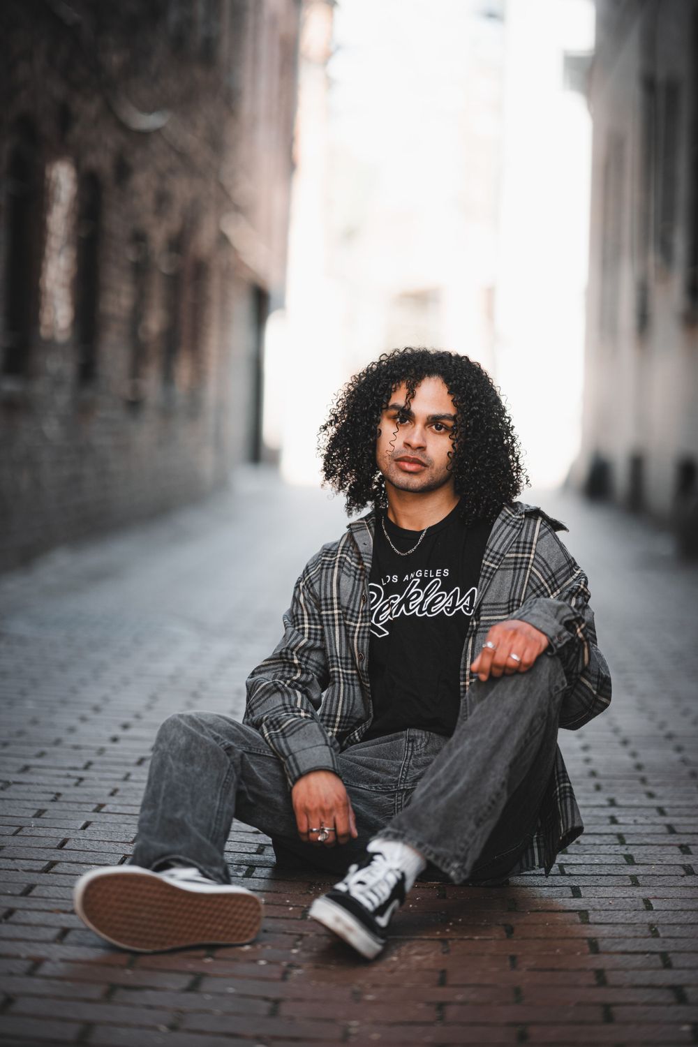 Portrait of a model with curly hair wearing a plaid jacket sitting on a cobblestone street in an urban setting in DuPont Circle.