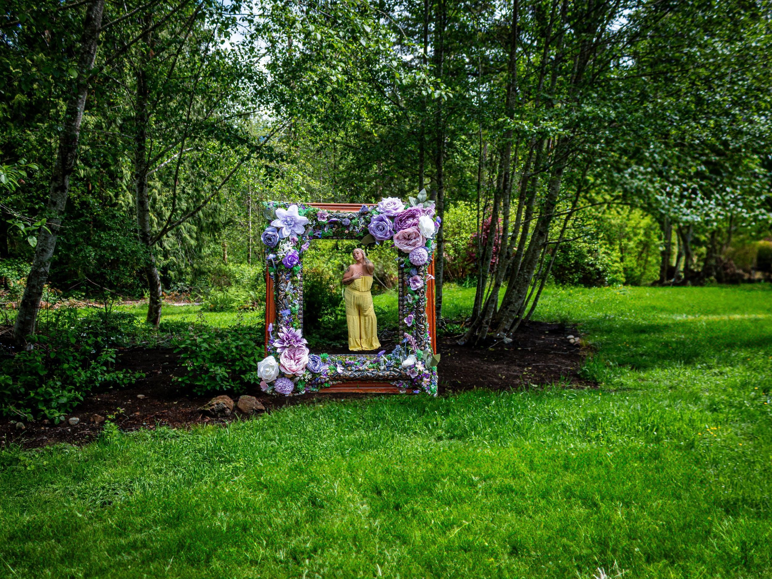 A decorative purple and floral frame floats in a lush green garden setting, framing a woman in yellow.