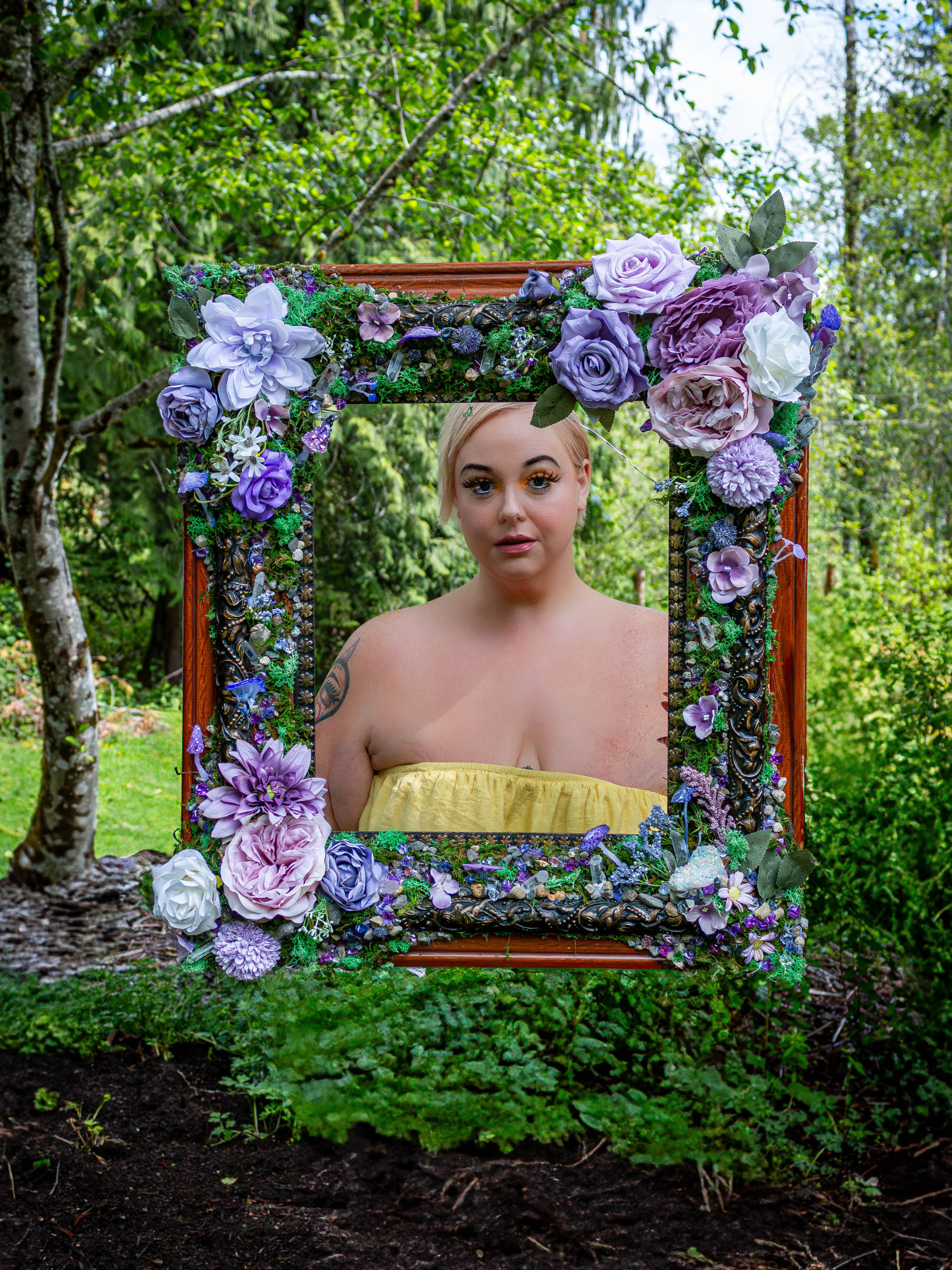 Creative portrait through wooden frame decorated with purple and pink flowers in lush forest setting.