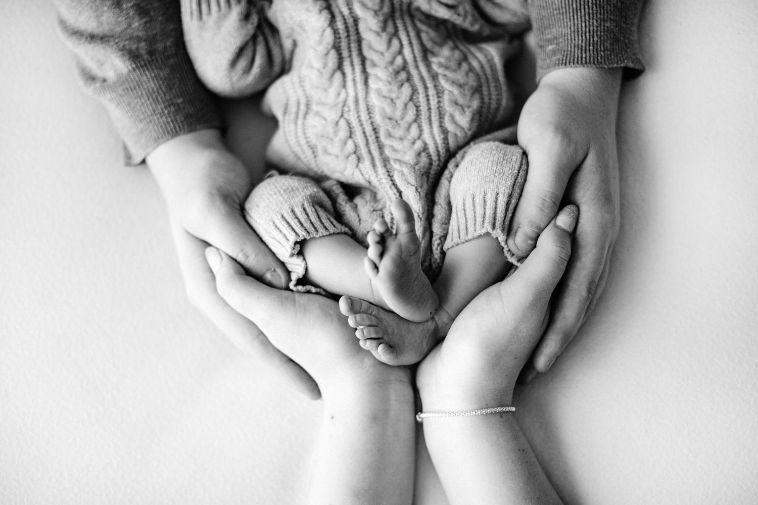 Black and white close-up of adult hands gently holding baby feet at newborn photoshoot in mansfield, nottinghamshire