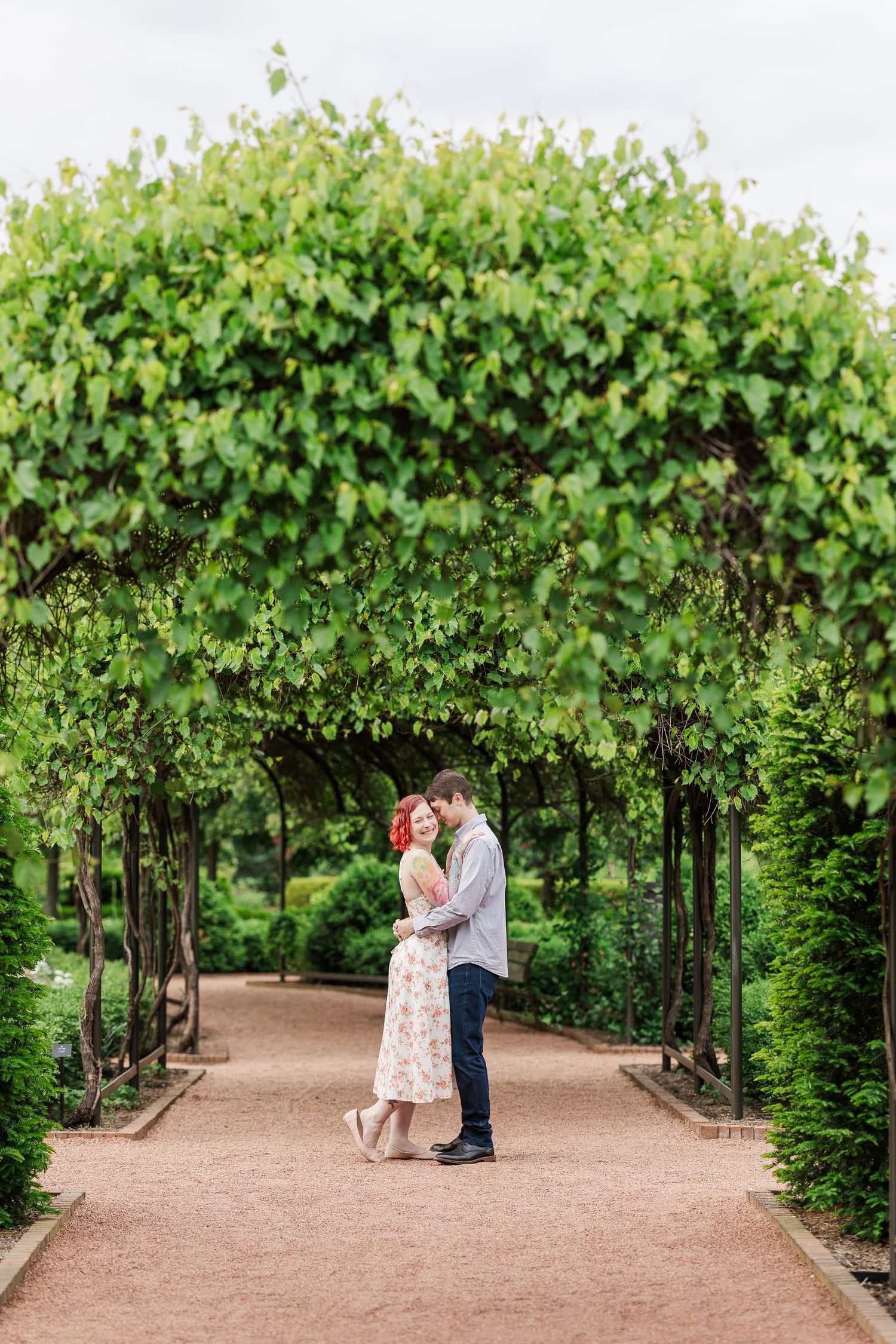 A couple embraces on a romantic garden path under a lush green vine archway at Cantigny Park