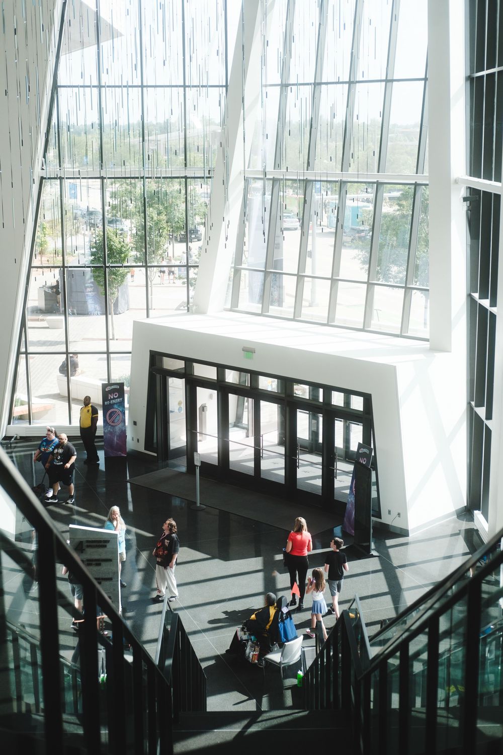 People walking down stairs in a modern building interior with large angled windows and natural lighting.