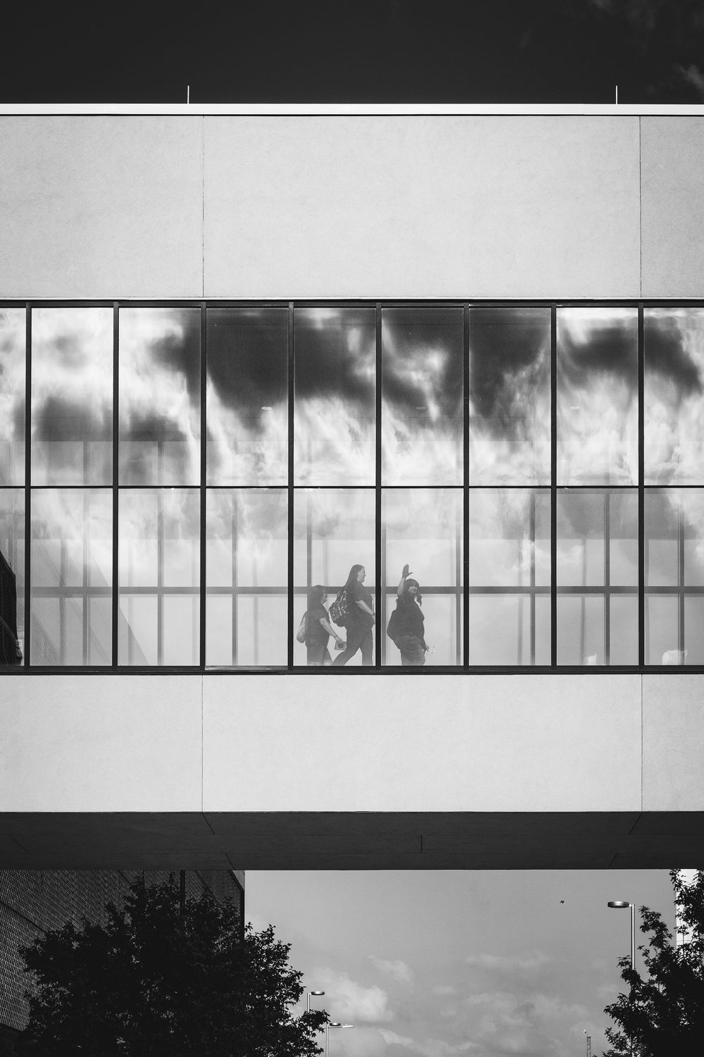 Silhouettes of people visible through large office windows against dramatic stormy clouds in black and white photography.