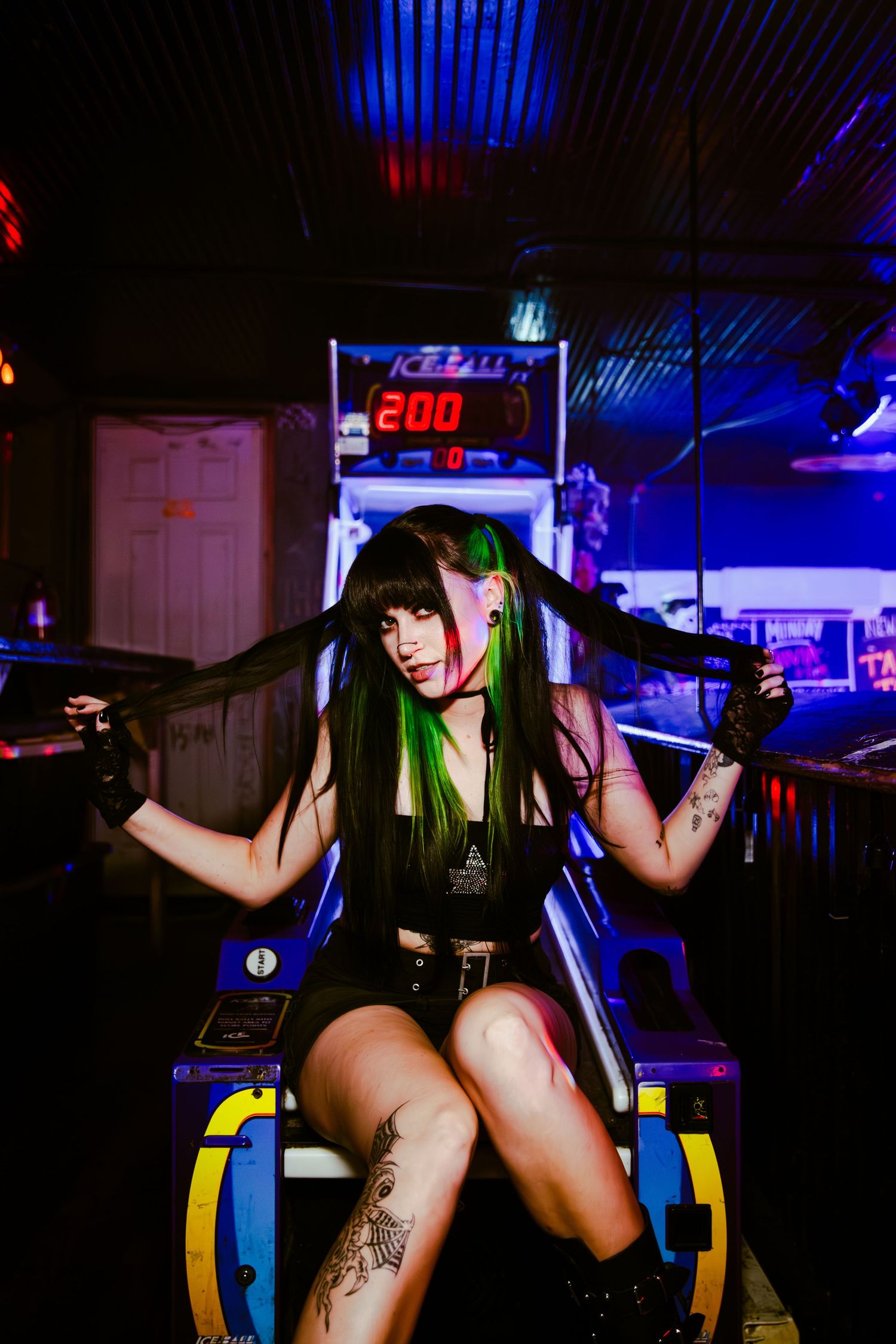 Cosplayer with green hair poses playfully in an arcade with neon lighting and game machines in the background.