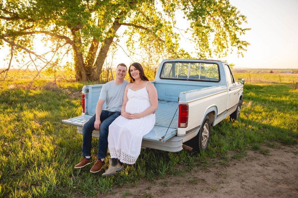 A vintage blue pickup truck parked under a sunlit tree in a golden meadow during sunset.