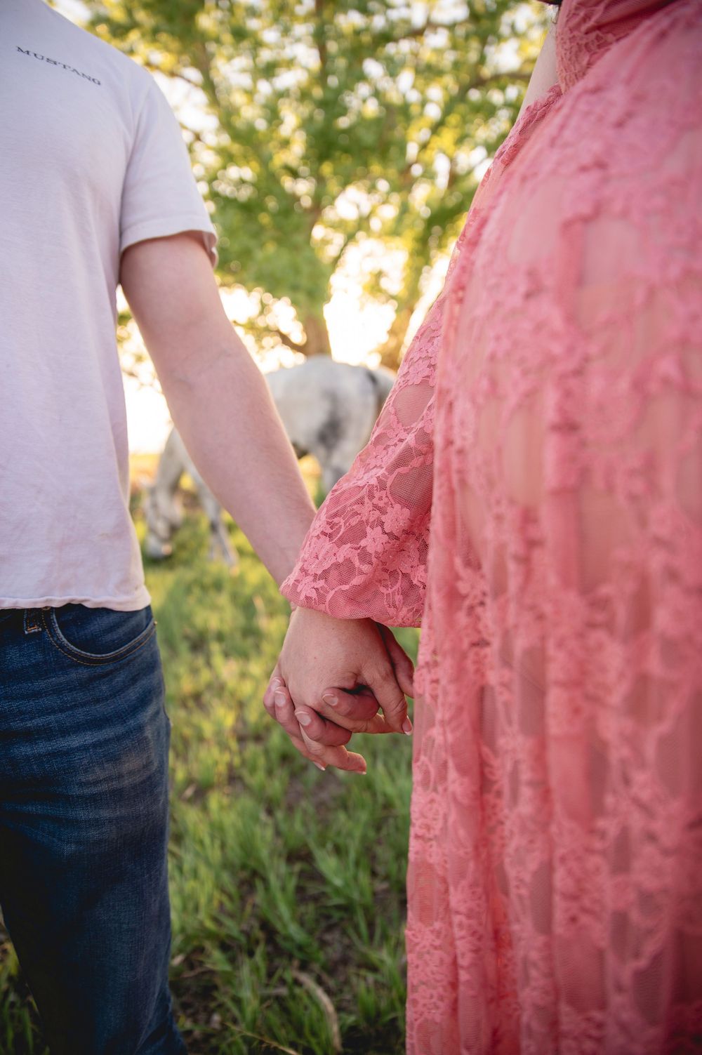 A couple holding hands in a sunset garden, with one wearing jeans and white shirt and the other in a coral lace dress.