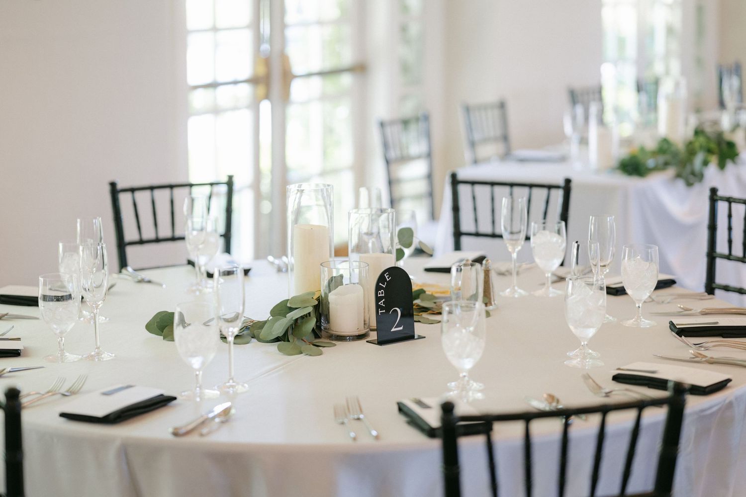 Elegant wedding reception hall with arched windows, white tablecloths, and ornate wall sconces creating a romantic atmosphere.